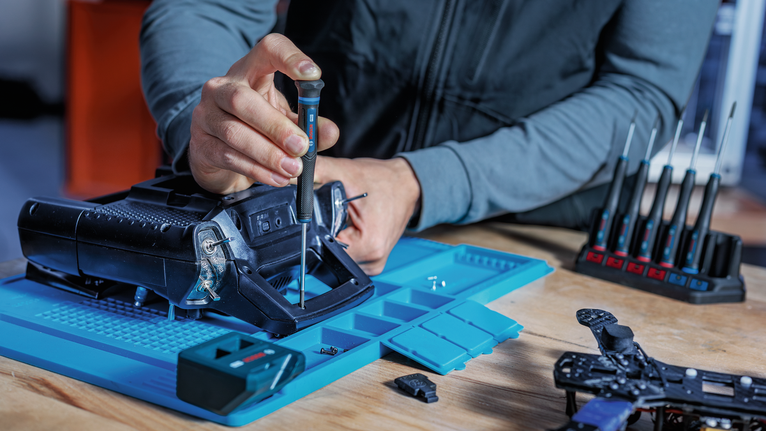 يقوم شخص بتجميع جهاز على محطة عمل زرقاء باستخدام مفك براغي.