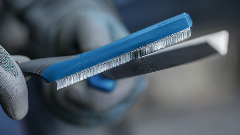 شخص يرتدي معدات السلامة يمسك مبرد شحذ بالقرب من حافة أداة معدنية.