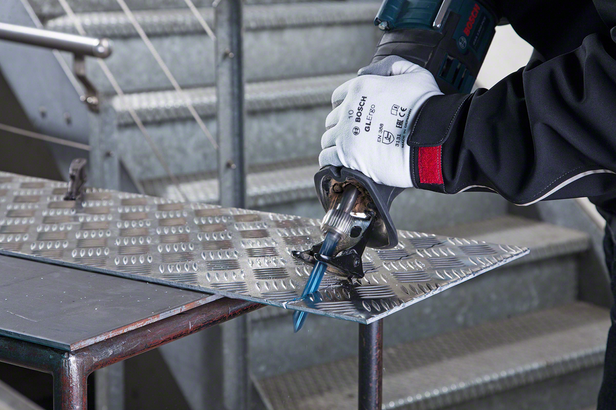 Person wearing safety equipment cuts metal sheet with a reciprocating saw.