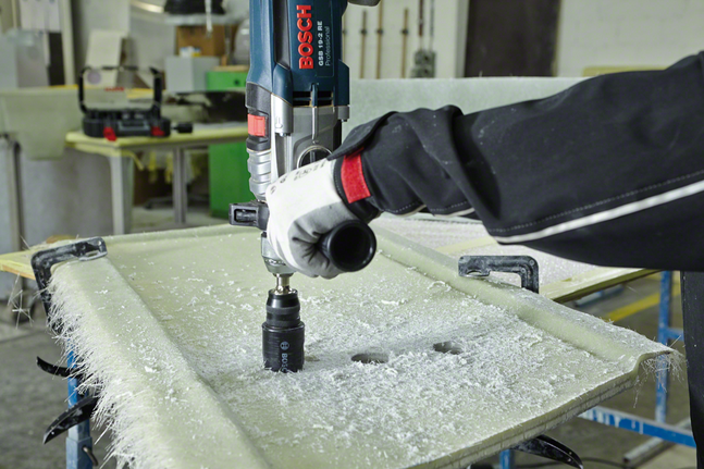 Person wearing safety equipment drills a hole in a fiberglass panel.