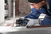 A person wearing safety equipment uses a multi-cutter to trim copper pipes on a dusty floor.