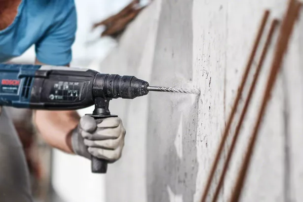 Person wearing safety equipment drills into a concrete wall.
