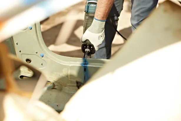 Person wearing safety equipment uses a reciprocating saw to cut metal in a vehicle frame.