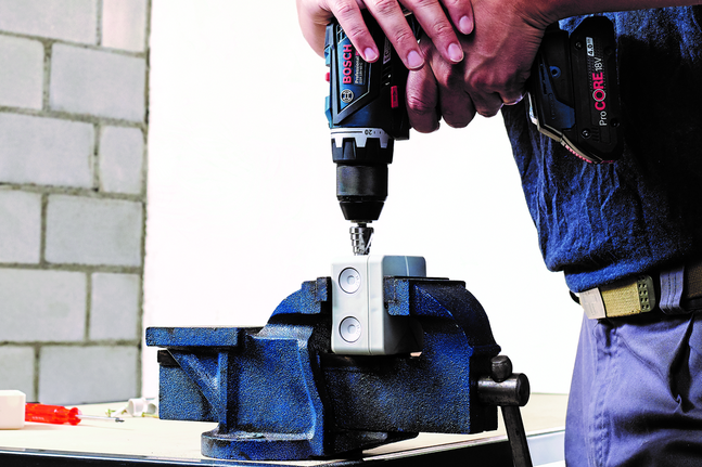 Person using a cordless drill to work on a metal part secured in a vise.