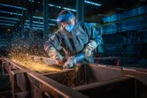A person wearing safety equipment grinds metal, creating a shower of sparks.