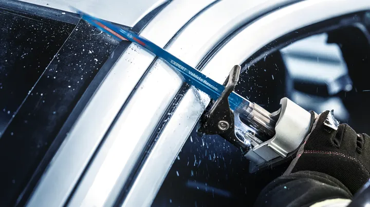 Person wearing safety equipment uses a reciprocating saw to cut through a car frame.