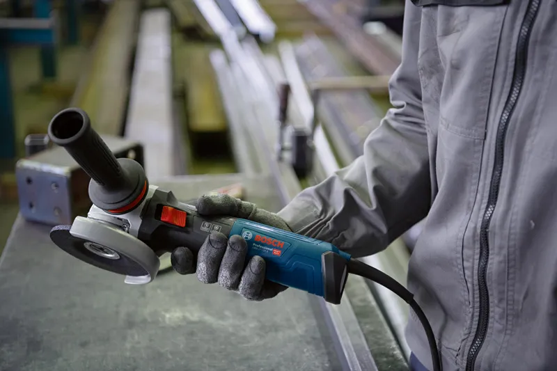 A person wearing safety equipment holds an angle grinder in a workshop.