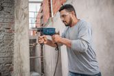 A person wearing safety equipment drills into a concrete wall with an impact drill.