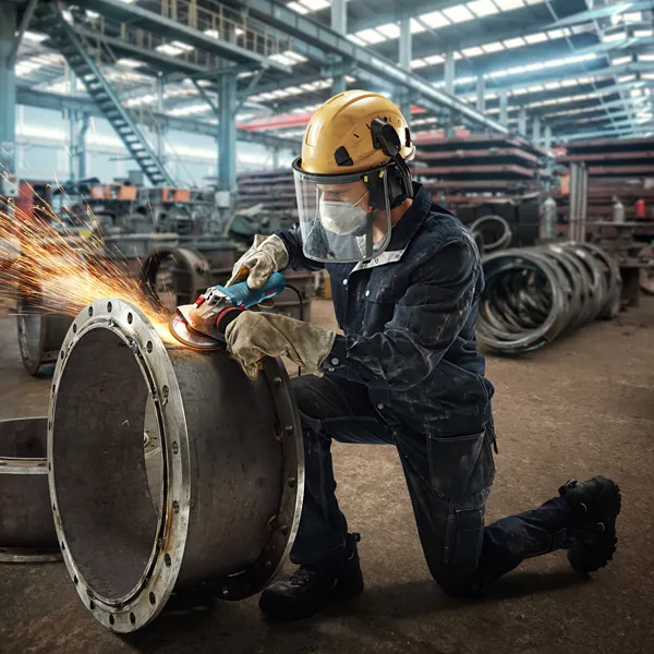 A person wearing safety equipment grinds the edge of a large metal pipe, producing sparks.