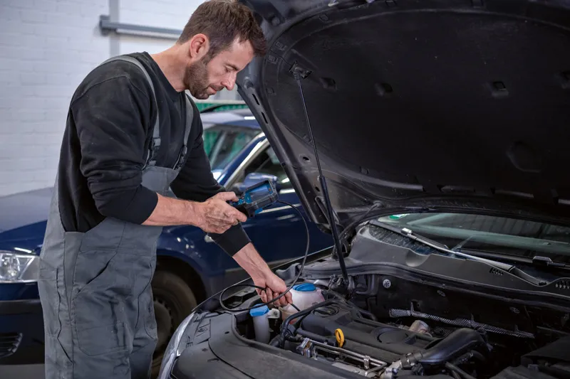 A person inspects a car engine using an inspection camera in a workshop.
