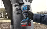 A person wearing safety equipment uses a cordless impact wrench on a steel structure.