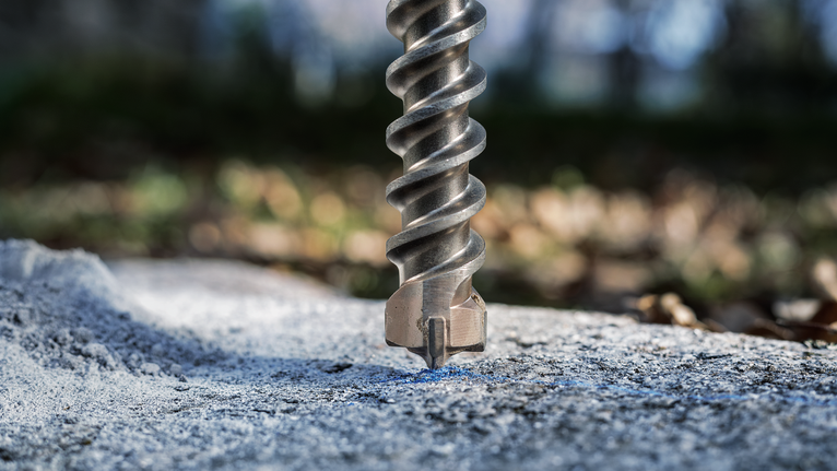 Large masonry drill bit boring into concrete outdoors.