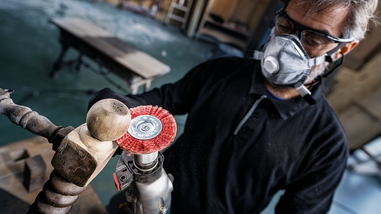 Person wearing safety equipment polishes a wooden spindle with a power tool.