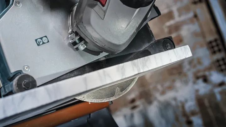 Cutting machine slices through a slab of marble in a workshop setting.