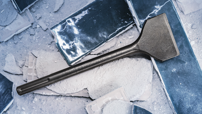 Wide chisel rests on broken concrete slabs covered in dust.