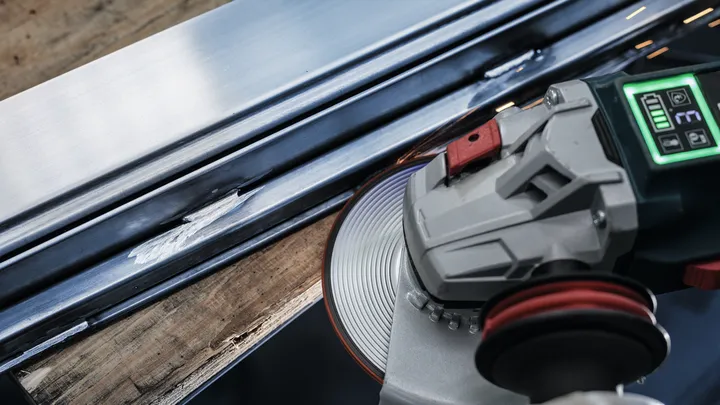 Angle grinder smoothing the edge of a metal beam.