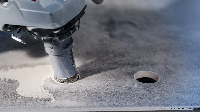 A power tool with a diamond hole saw drills through a stone slab.