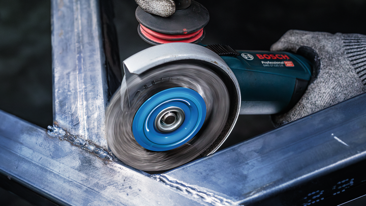 Person wearing safety equipment grinds a metal frame with an angle grinder.