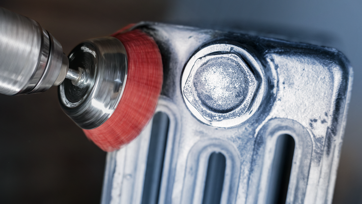 Wire brush wheel polishes a metal surface near a large bolt.