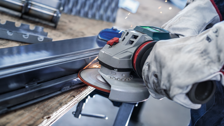 A person wearing safety equipment grinds a metal beam with an angle grinder.