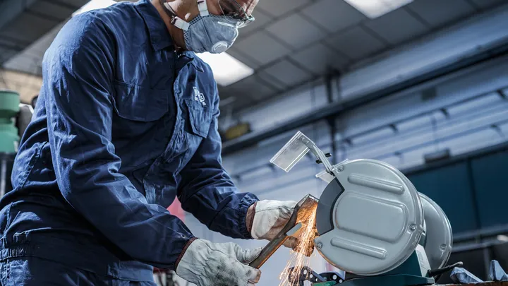 Person wearing safety equipment uses a metal cutting saw to cut a pipe, producing sparks.