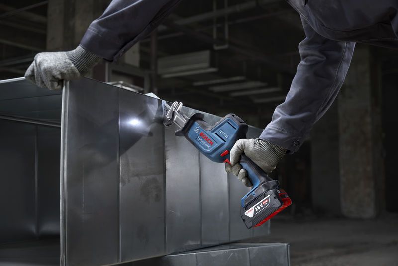 A person wearing safety equipment cuts sheet metal with a cordless reciprocating saw.