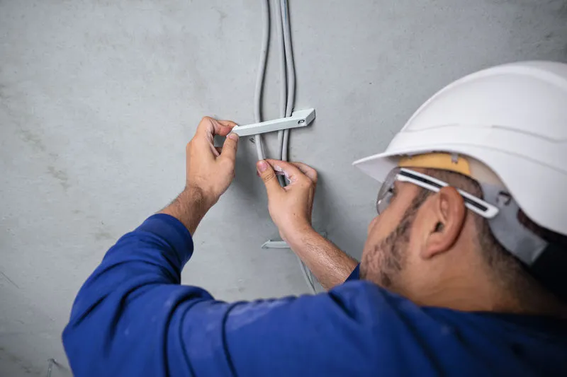 A person wearing safety equipment secures electrical cables to a ceiling.