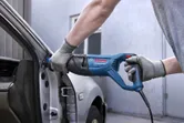 A person wearing safety equipment uses a reciprocating saw to cut part of a car door.