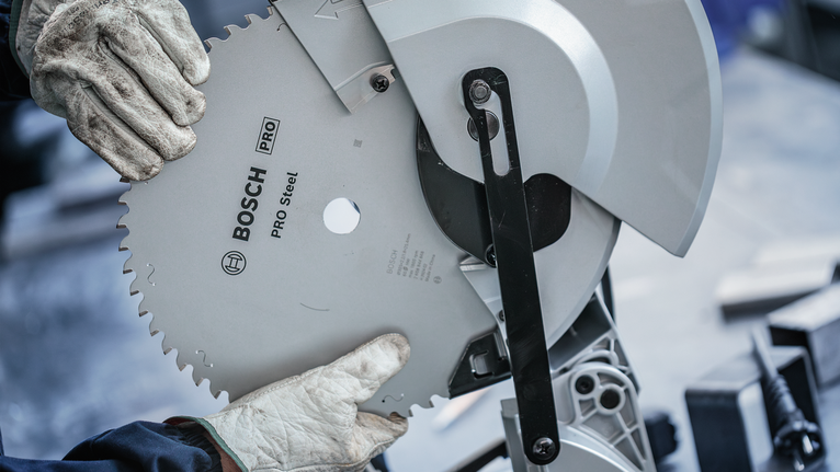 Person wearing safety equipment installs a circular saw blade on a metal cutting machine.