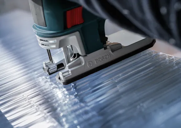 Jigsaw cutting clear acrylic sheet along straight lines.