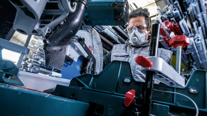 Person wearing safety equipment operates a circular saw in a workshop.