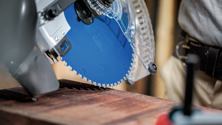 Person wearing safety equipment operates a circular saw on a wooden plank.