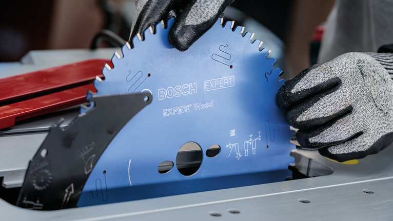 Person wearing safety equipment installs a circular saw blade into a table saw.