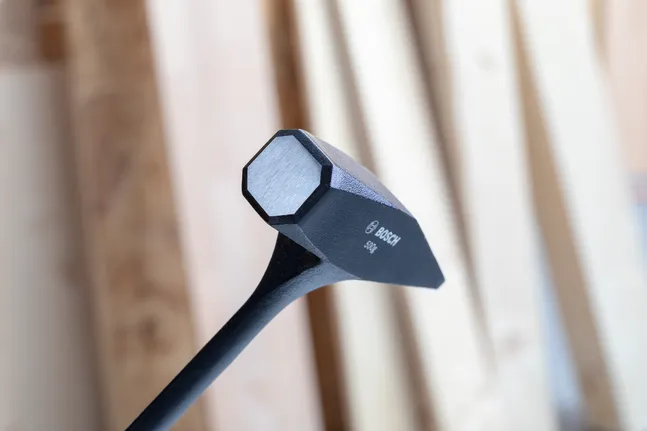 Black sledgehammer head close up with wooden planks in the background.