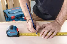 Person marking a measurement on wood with a tape measure and pencil.