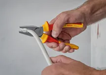 Person uses insulated pliers to grip a thick cable.