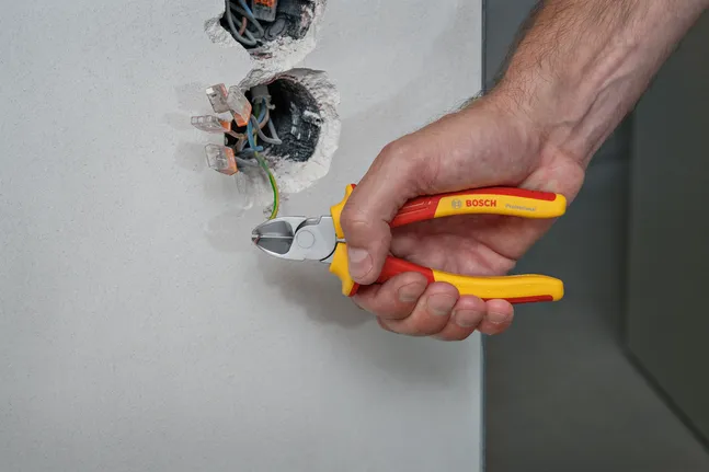 Person cuts electrical wire with insulated pliers near exposed wiring.