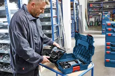 A person in a workshop opens a blue tool case with power tools inside.
