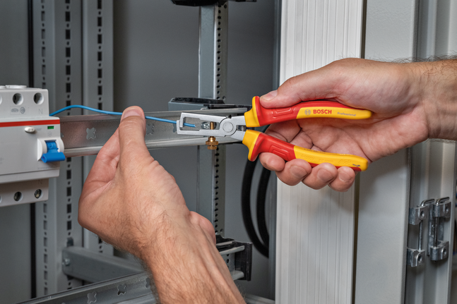 Person uses insulated pliers to grip electrical wire in a control panel.