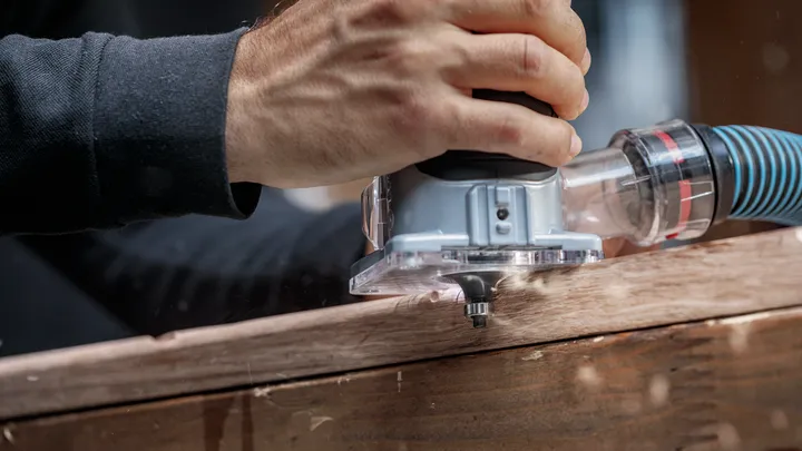 Person guides a power router along a wooden plank for precise edge shaping.