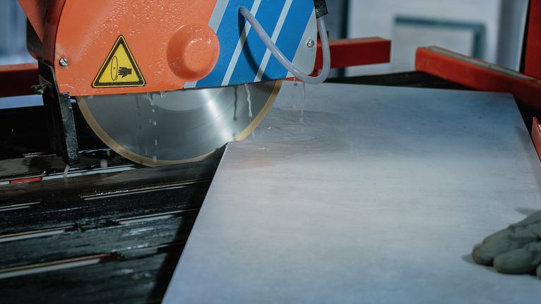 Person wearing safety equipment operates a wet saw to cut a large tile.