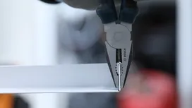 Person uses pliers to grip a metal strip.
