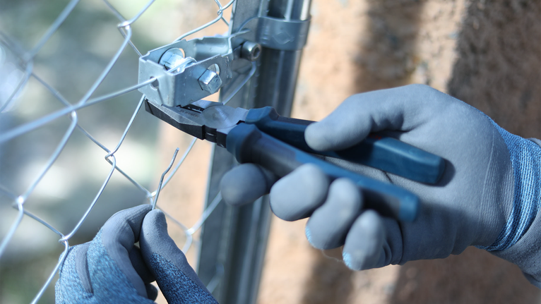 Person wearing safety equipment cuts metal fencing with pliers.