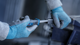 Person wearing safety equipment tightens a metal part with a screwdriver.