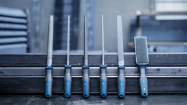 Six metal files with ergonomic handles are arranged on a steel workbench.