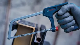 Person wearing safety equipment holds a hacksaw near a metal pipe.