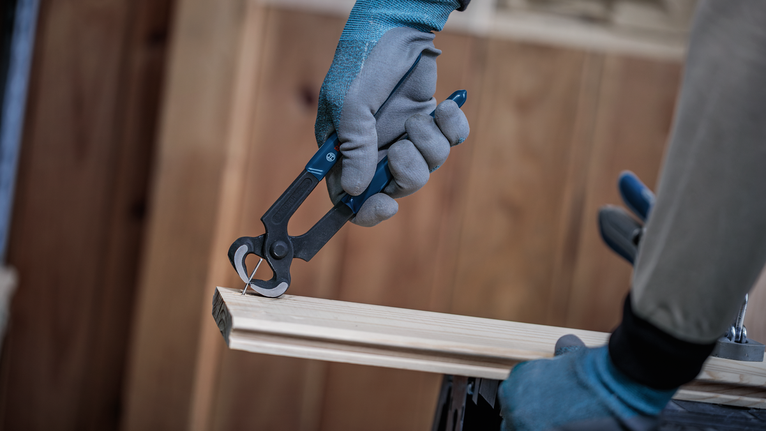 Person wearing safety equipment removes a nail from wood using pliers.