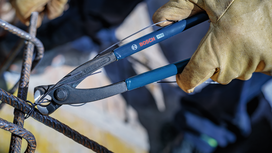 Person wearing safety equipment cuts wire on a metal frame with pliers.