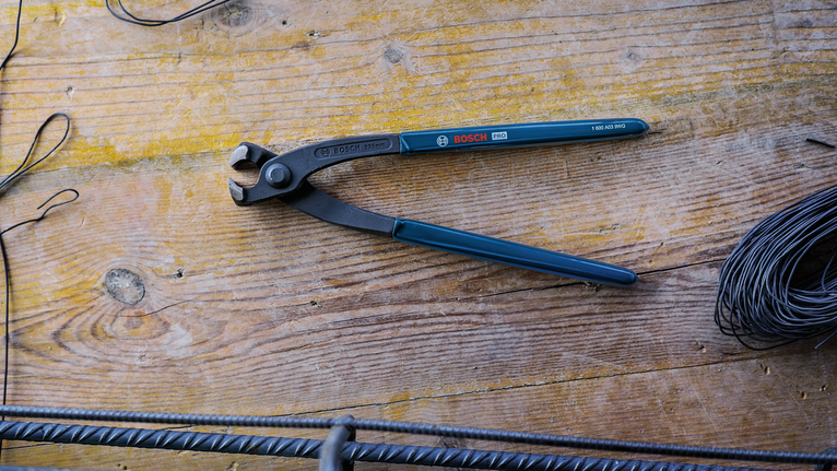 Cutting pliers on a wooden workbench beside rebar and coiled wire.