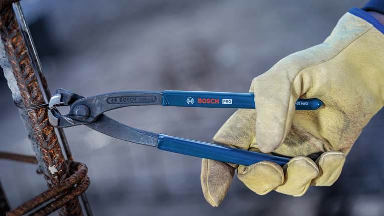 Person wearing safety equipment cuts thick wire on a metal frame with pliers.